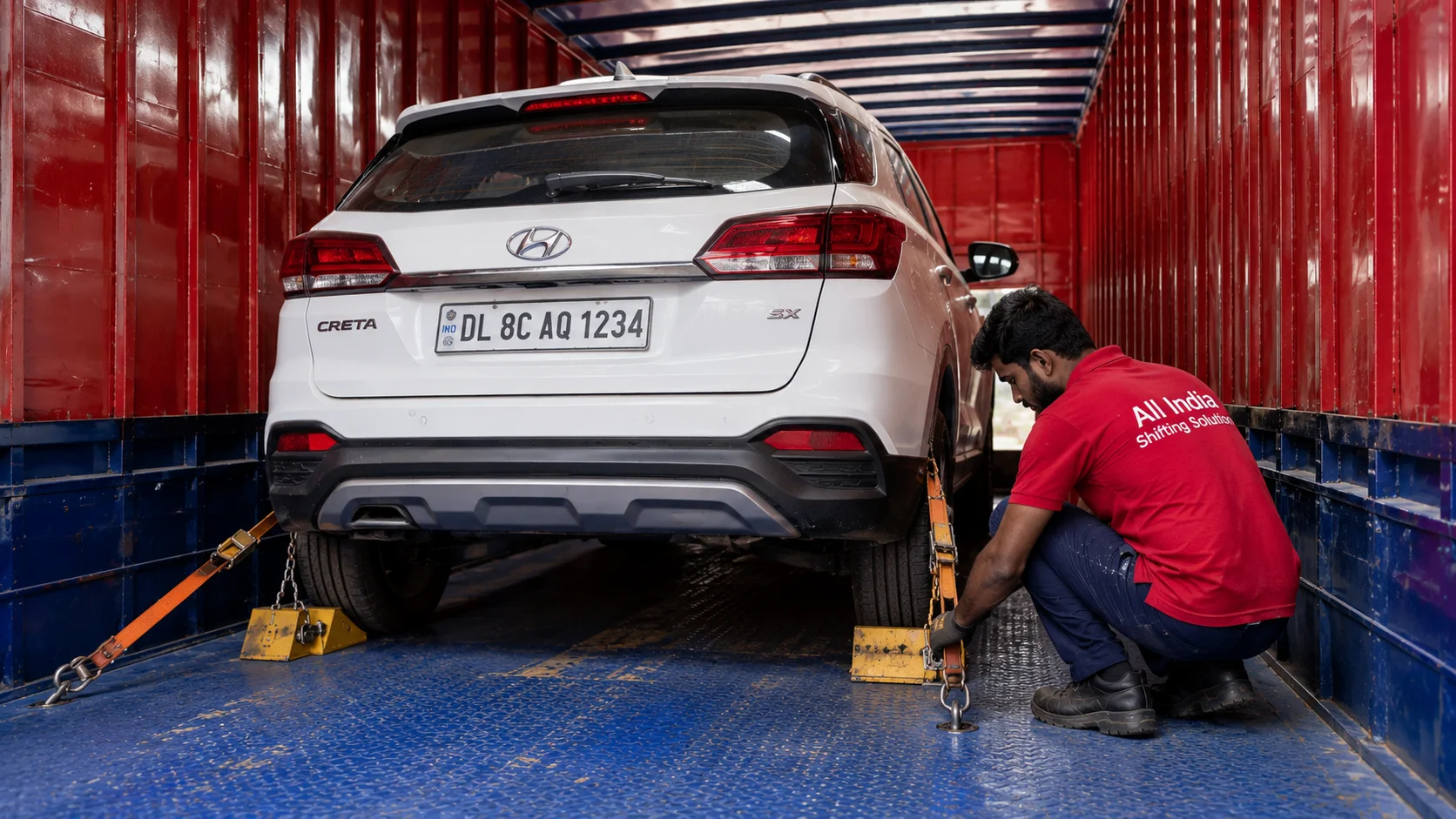 A detailed close-up of a worker checking the heavy wheel chocks and secure strapping of a car inside the well-lit interior of a plain red and blue Indian container truck with "All India Shifting Solution" in large black text.